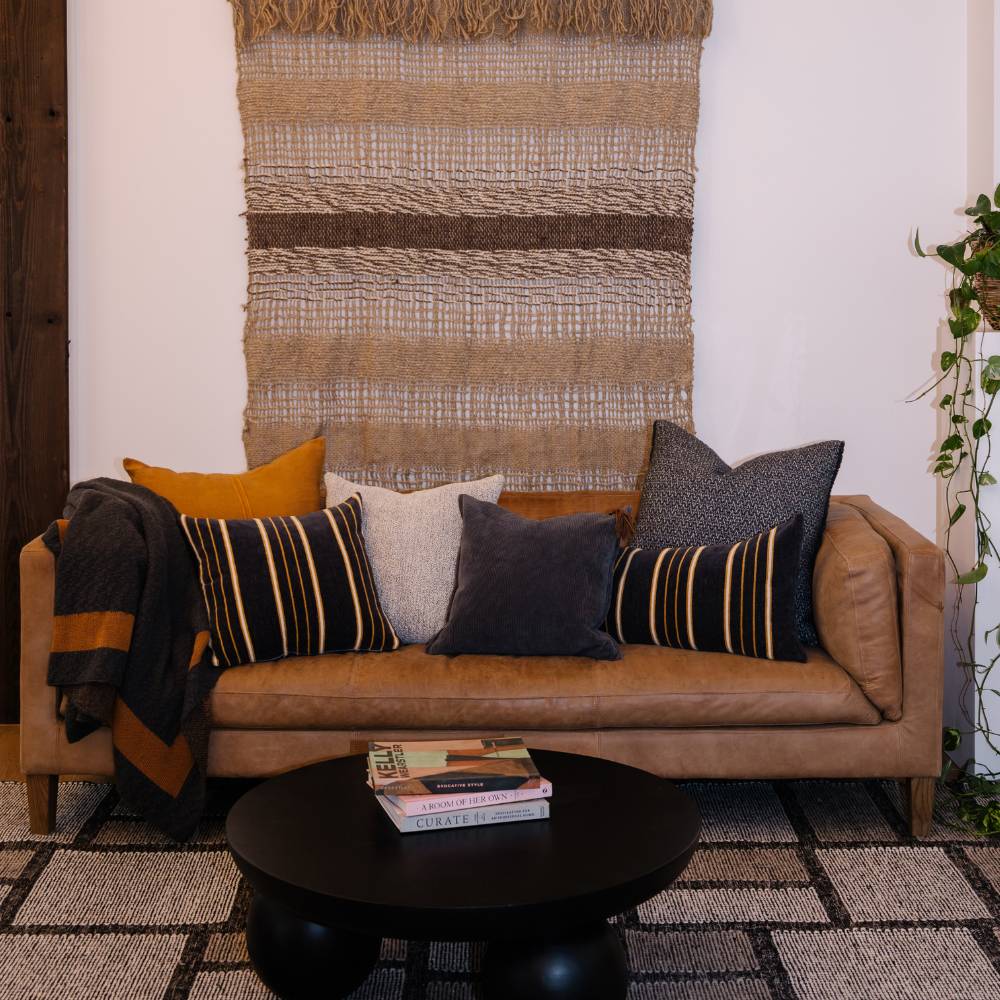 Brown leather sofa with colorful pillows in a living room setting.