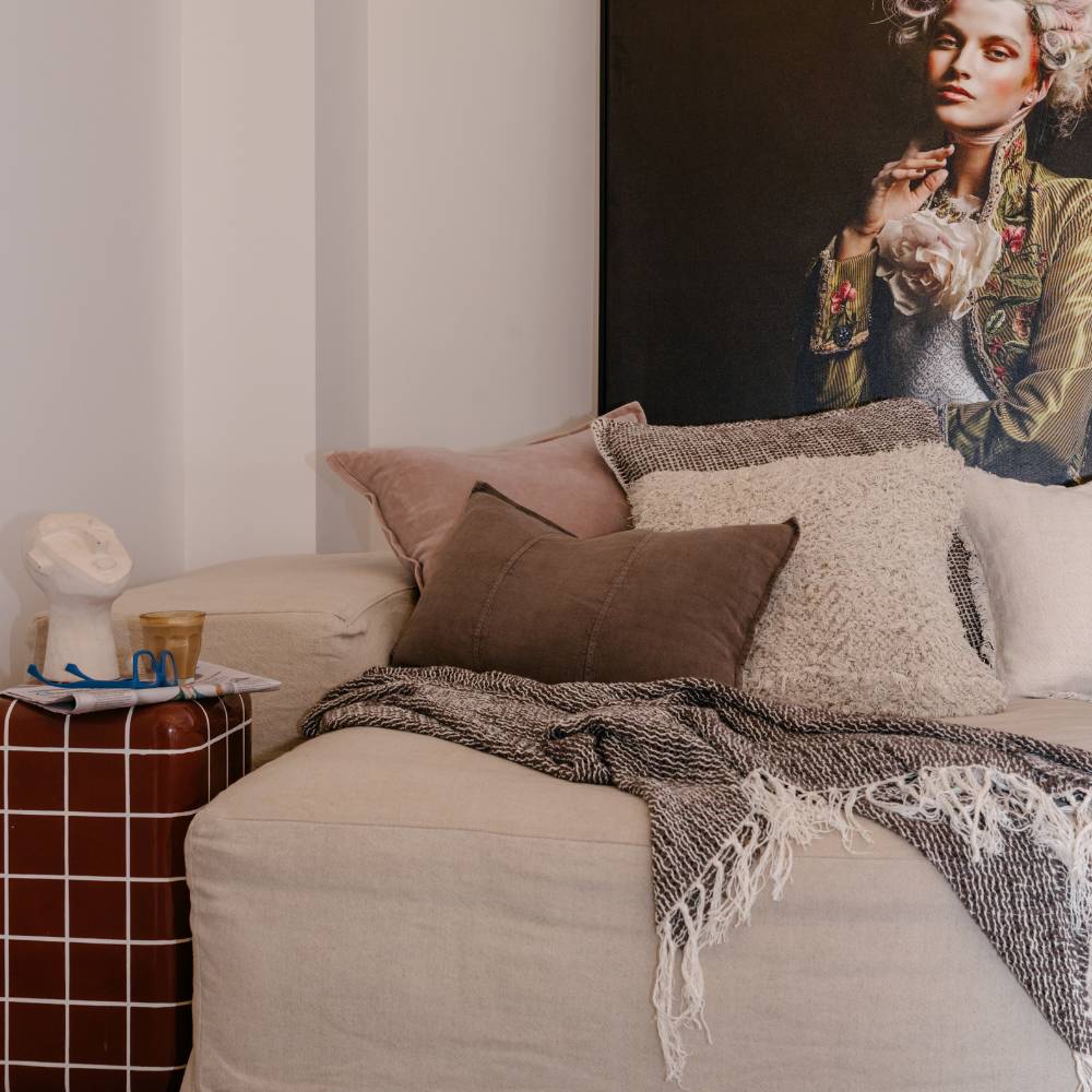 Neatly made sofa with decorative pillows and a throw, behind is a portrait of a person wearing floral outfit