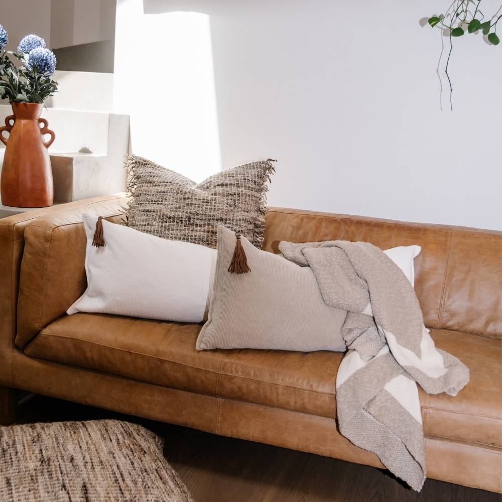 Brown leather sofa with decorative pillows and a blanket in a living room setting.