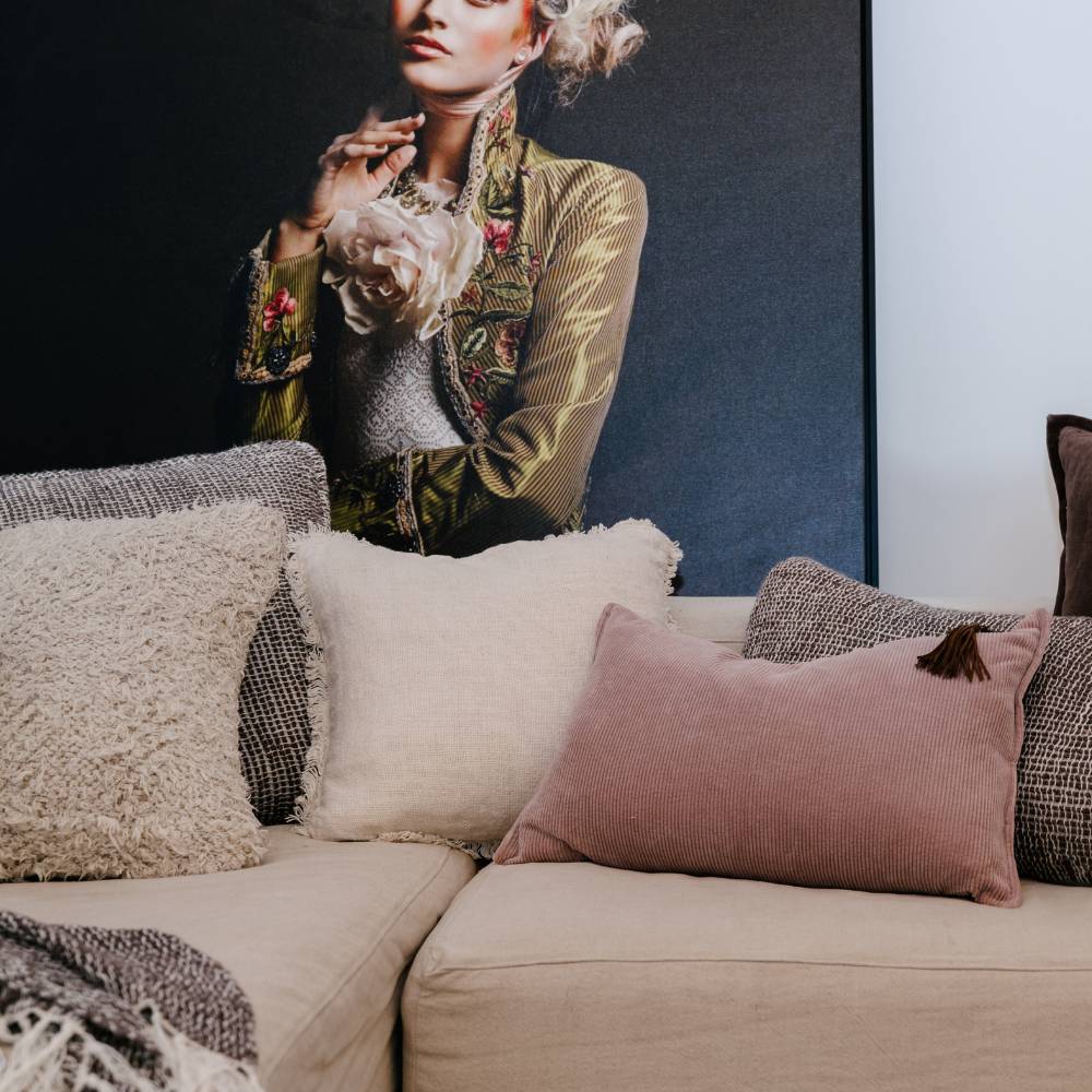 Beige sofa with decorative pillows and a portrait of a person in floral attire in the background.