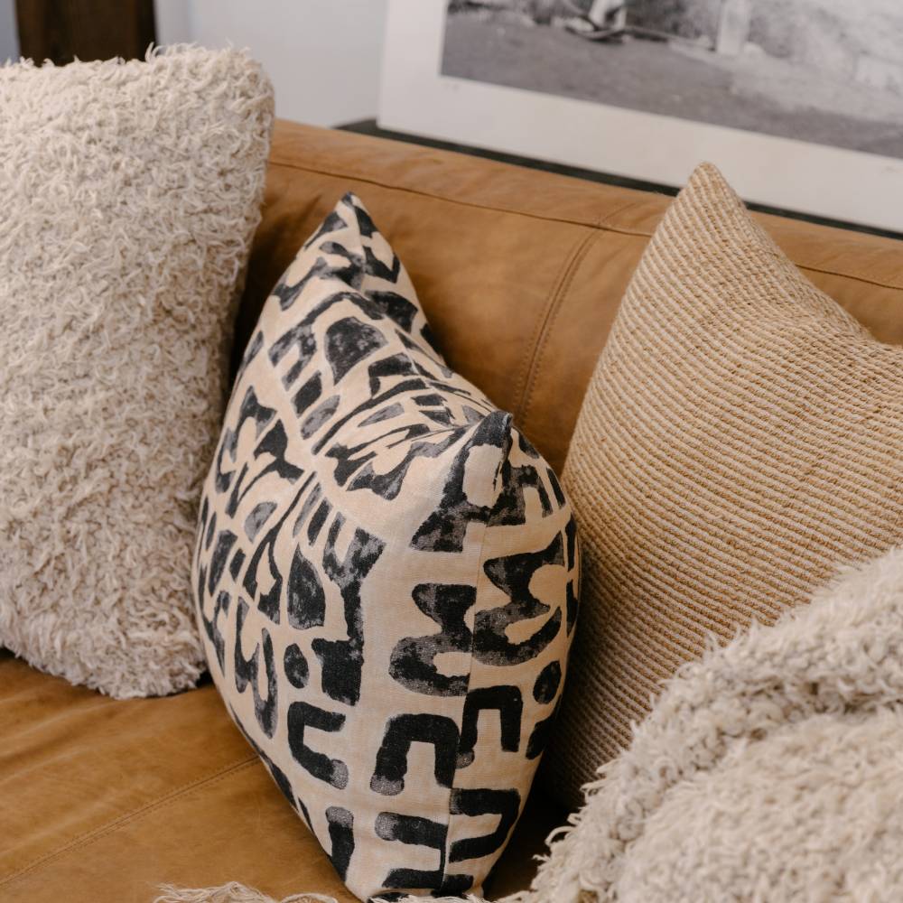 Patterned pillow on a brown leather sofa with other decorative pillows.