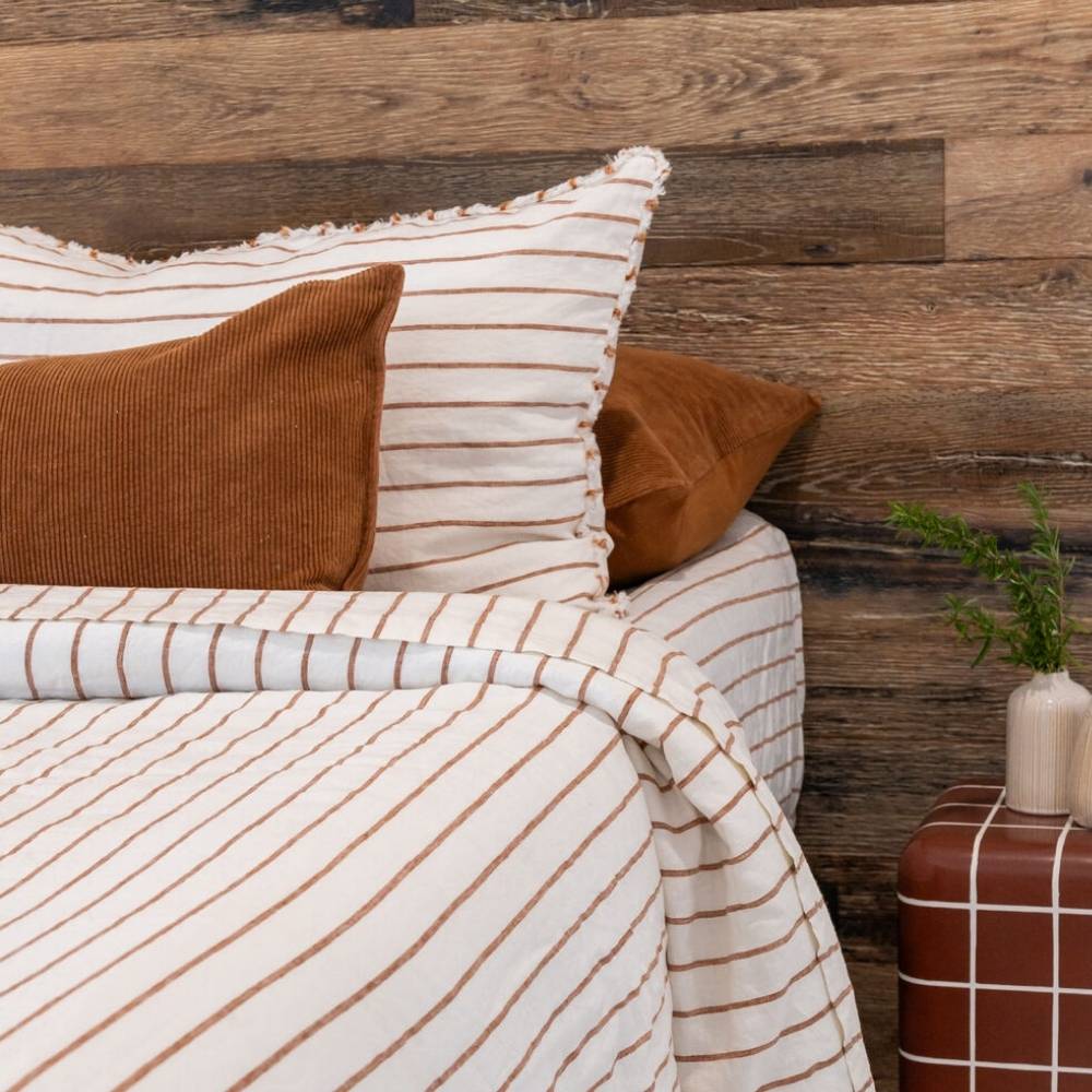 Striped bedding with brown and white pattern on a bed against a wooden wall.
