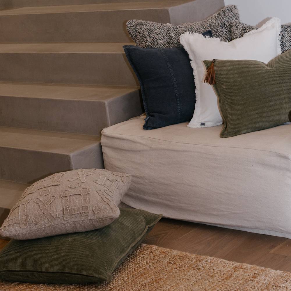 Couch with decorative pillows on a wooden floor next to a staircase