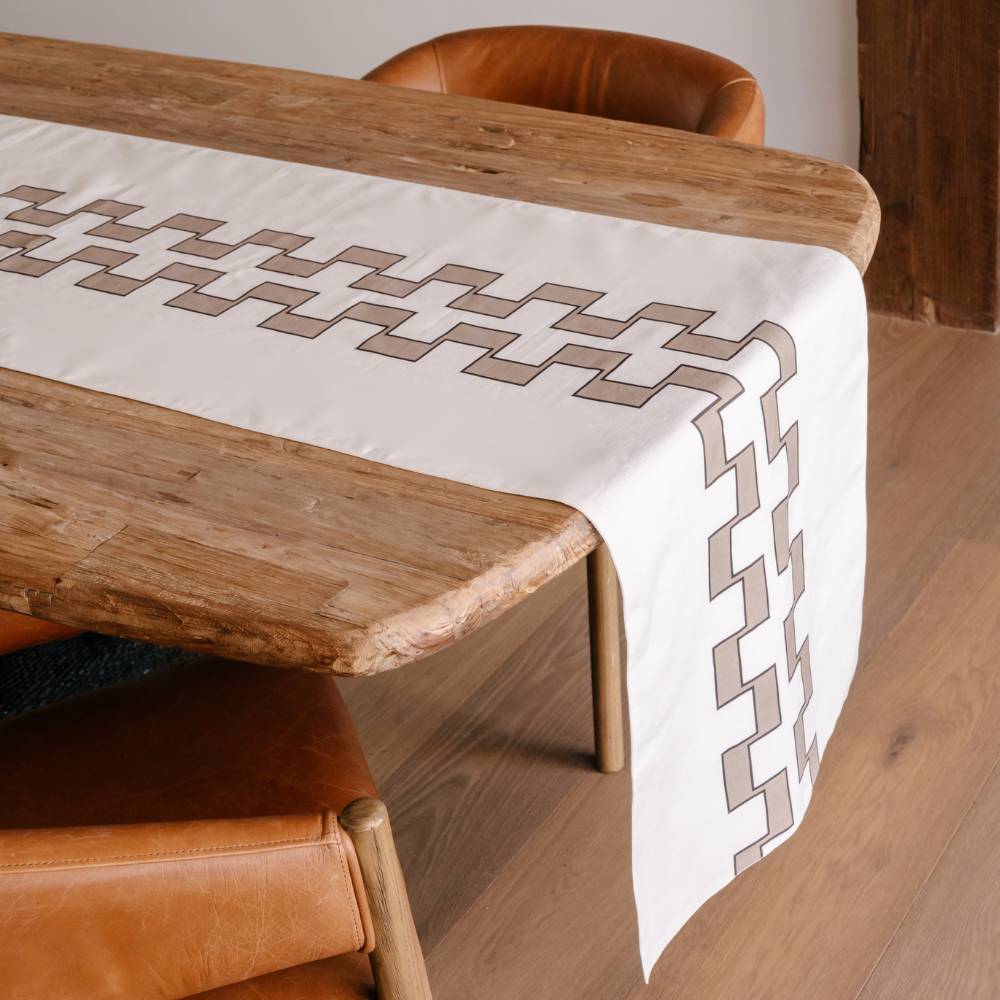 Wooden table with a patterned tablecloth and brown chairs.