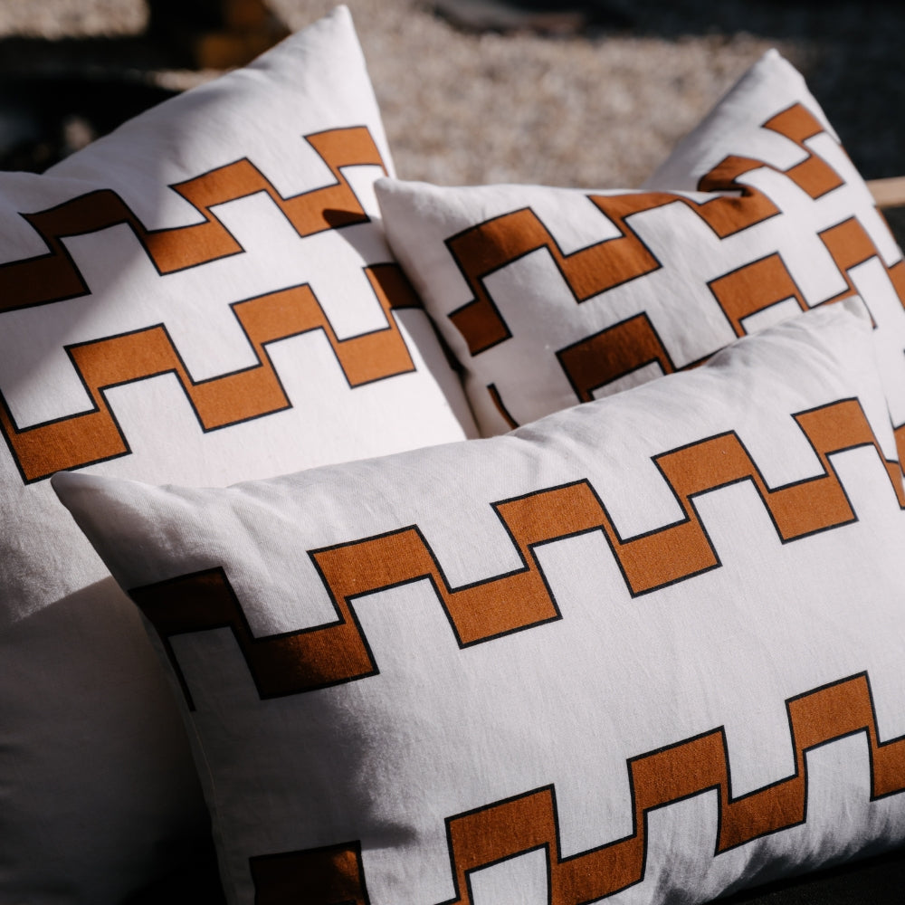 Three pillows with interlocking brown and white geometric pattern, outlined in black, outdoors.