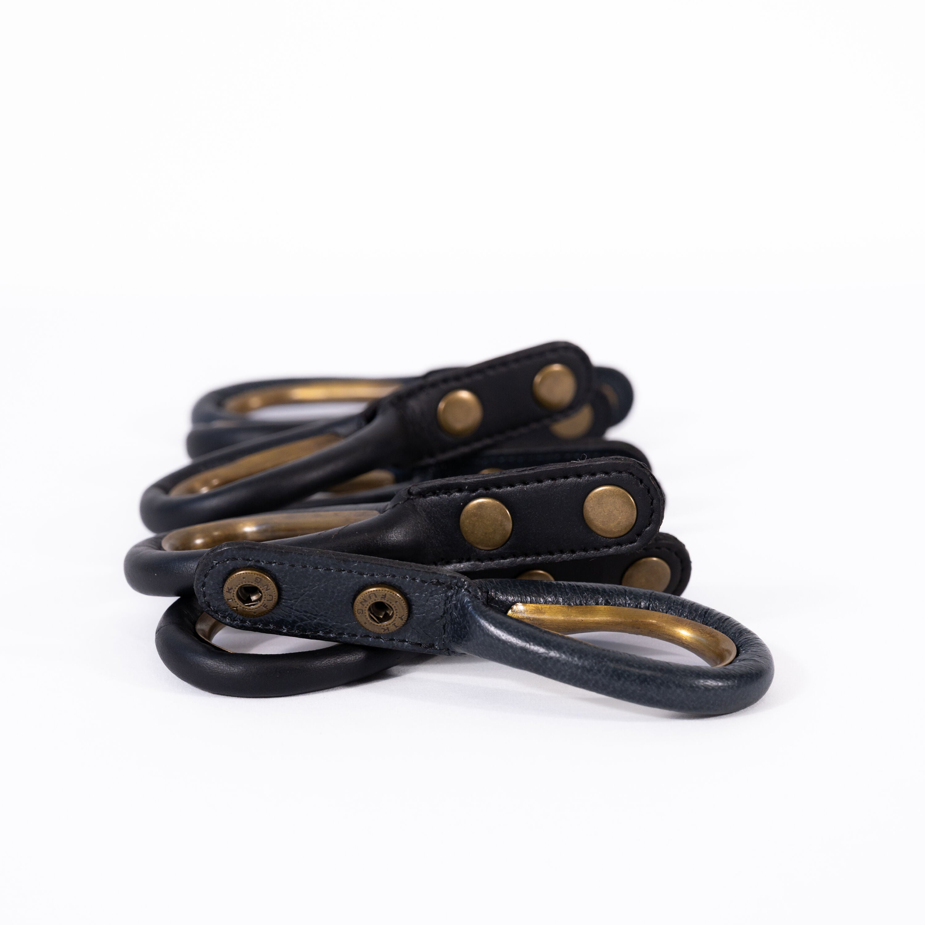 Set of black leather rings with antique brass-colored rings and rivets on a white background