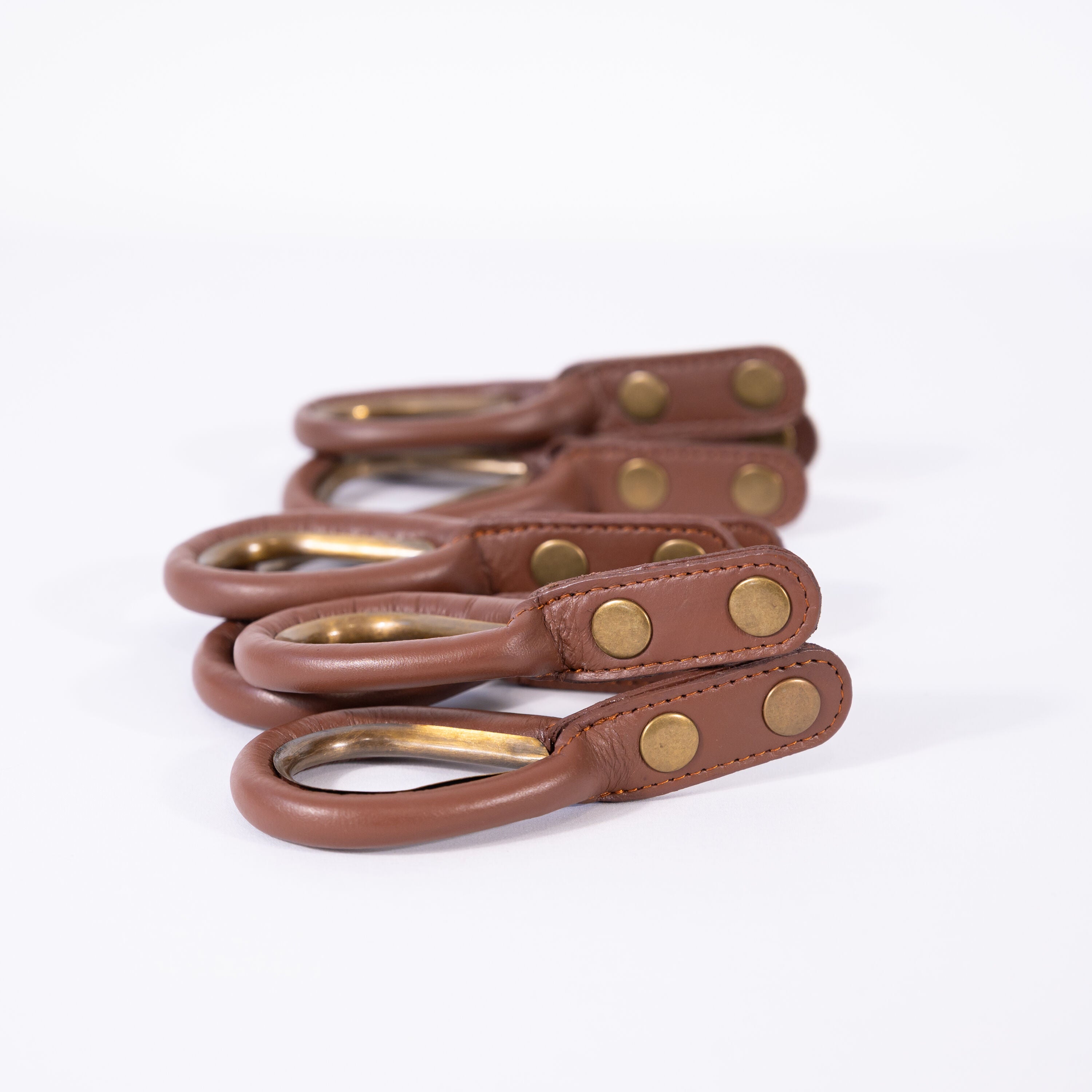 Set of brown leather rings with antique brass-colored rings and rivets on a white background