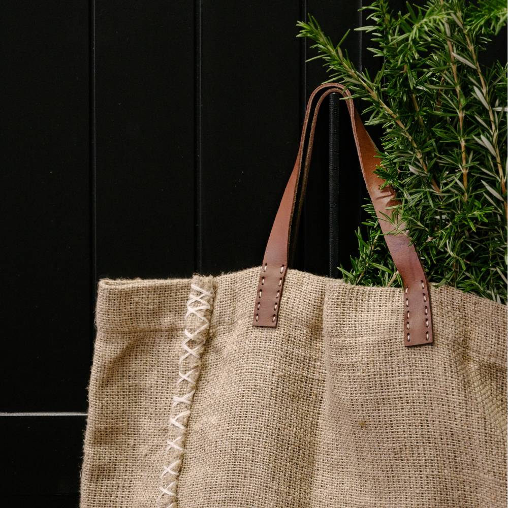 Jute tote bag with leather handles against a black background and a plant