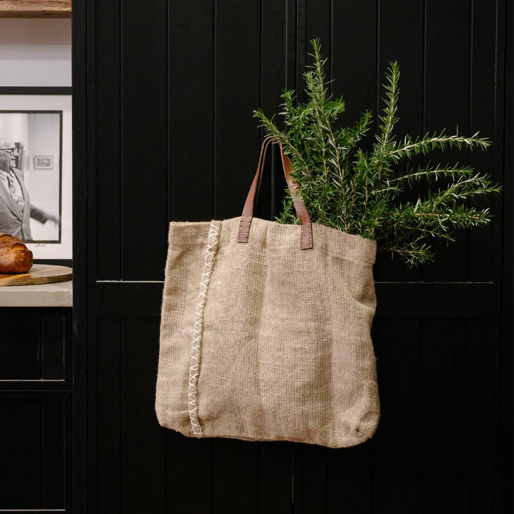 Jute tote bag with leather handles against a black background and a plant