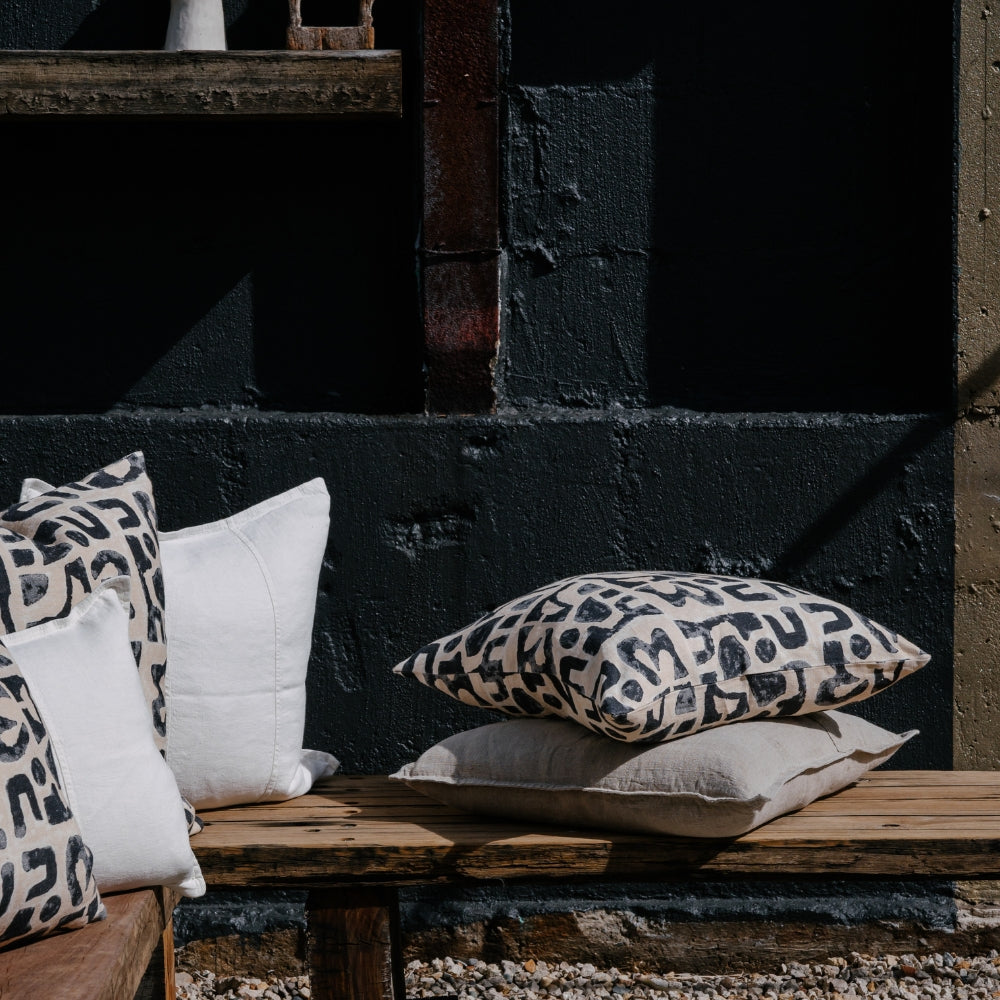 A collection of decorative pillows arranged on a rustic wooden bench, against a dark, textured wall.
