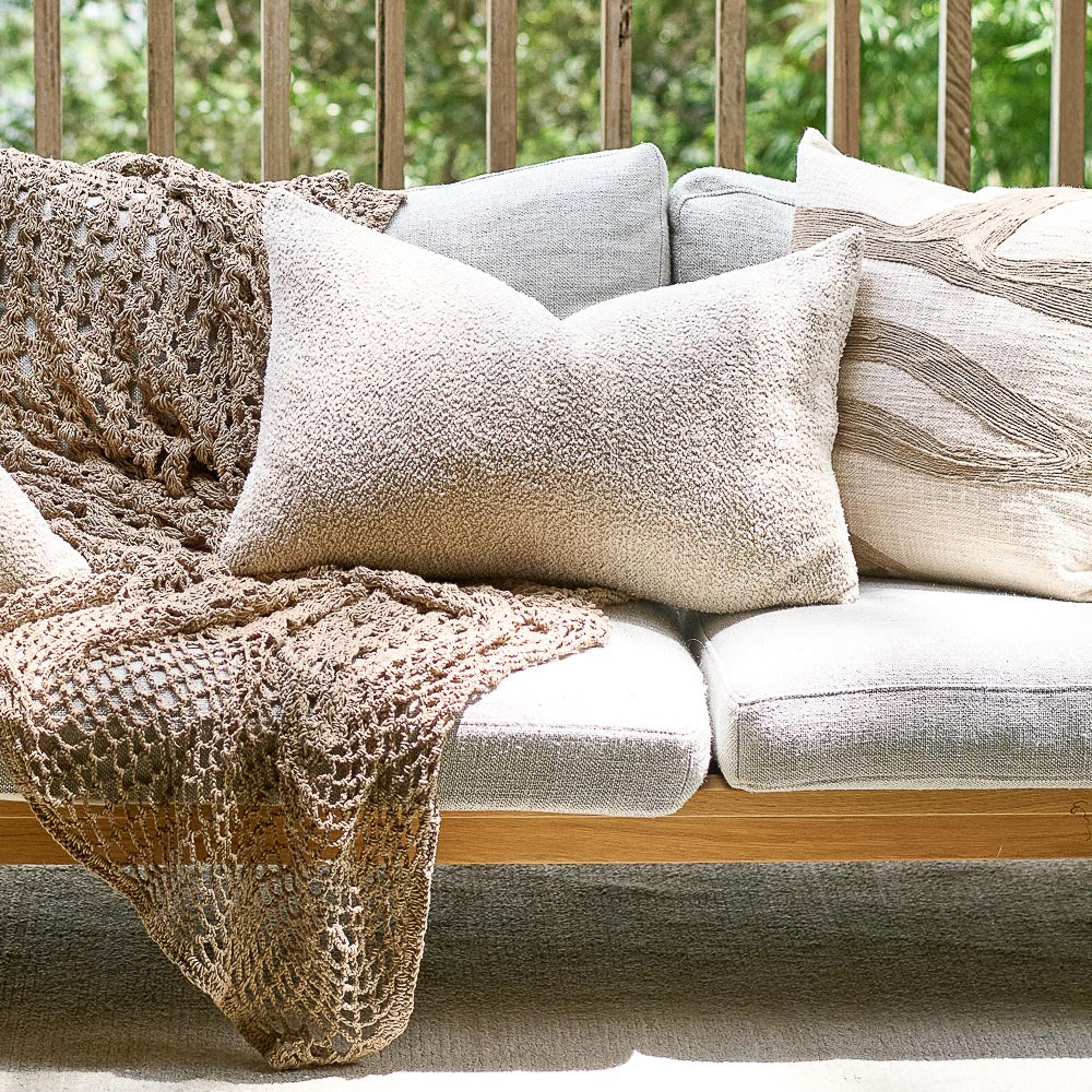 A beige cushion on a sofa with a brown throw