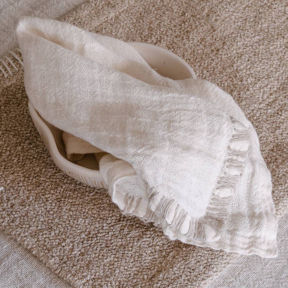 A white linen table napkin rests on a ceramic bowl on a rectangular tan placemat