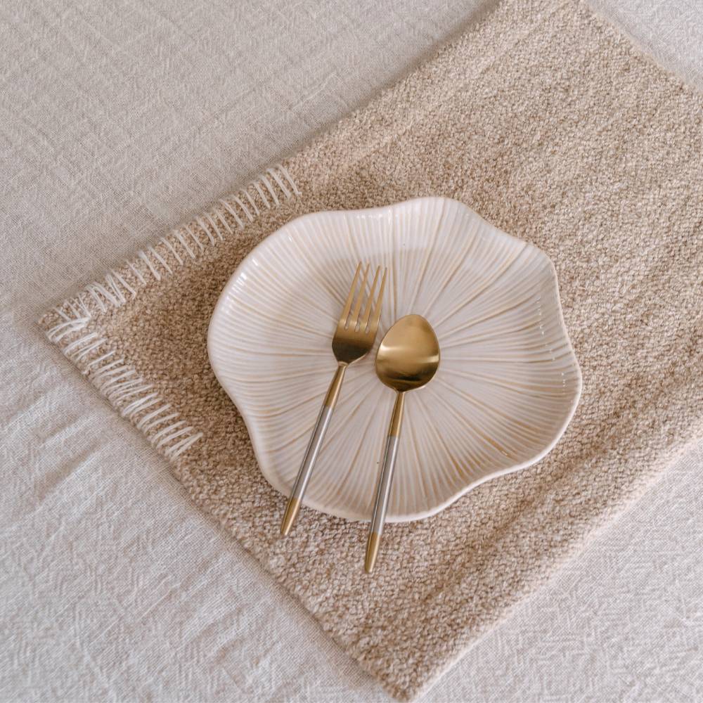 White ceramic plate with gold fork and spoon on a textured beige placemat.