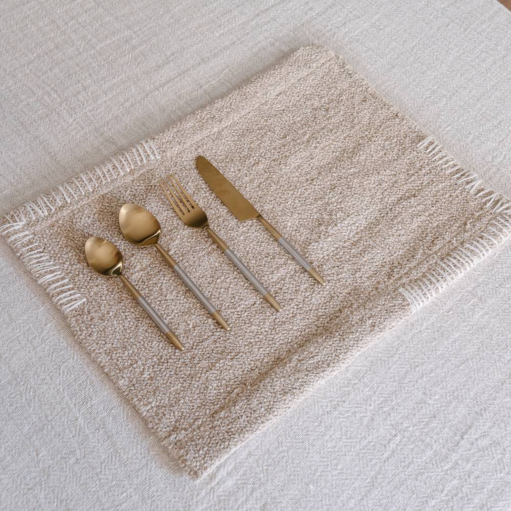 Set of gold cutlery on a textured beige placemat with a white background