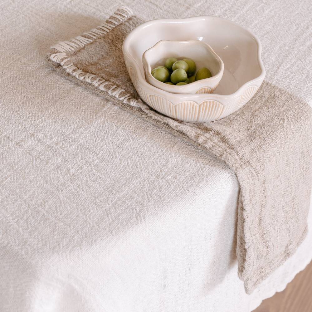 Beige textured tablecloth with a decorative bowl and green fruits on a neutral background