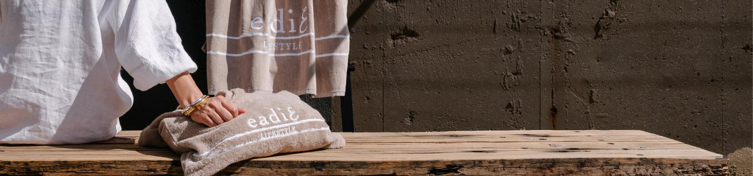 Person wearing gold and silver bangles with their hand on a natural terry-towelling tote. Eadie Beach towel hanging in the background.