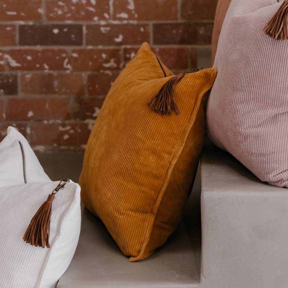 Three pillows with tassels on a surface against a brick wall.
