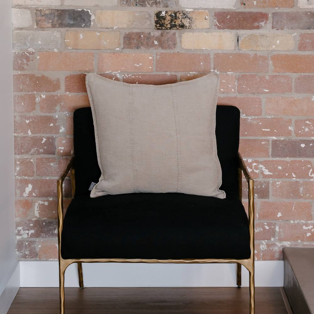 Black armchair with a beige pillow against a brick wall.