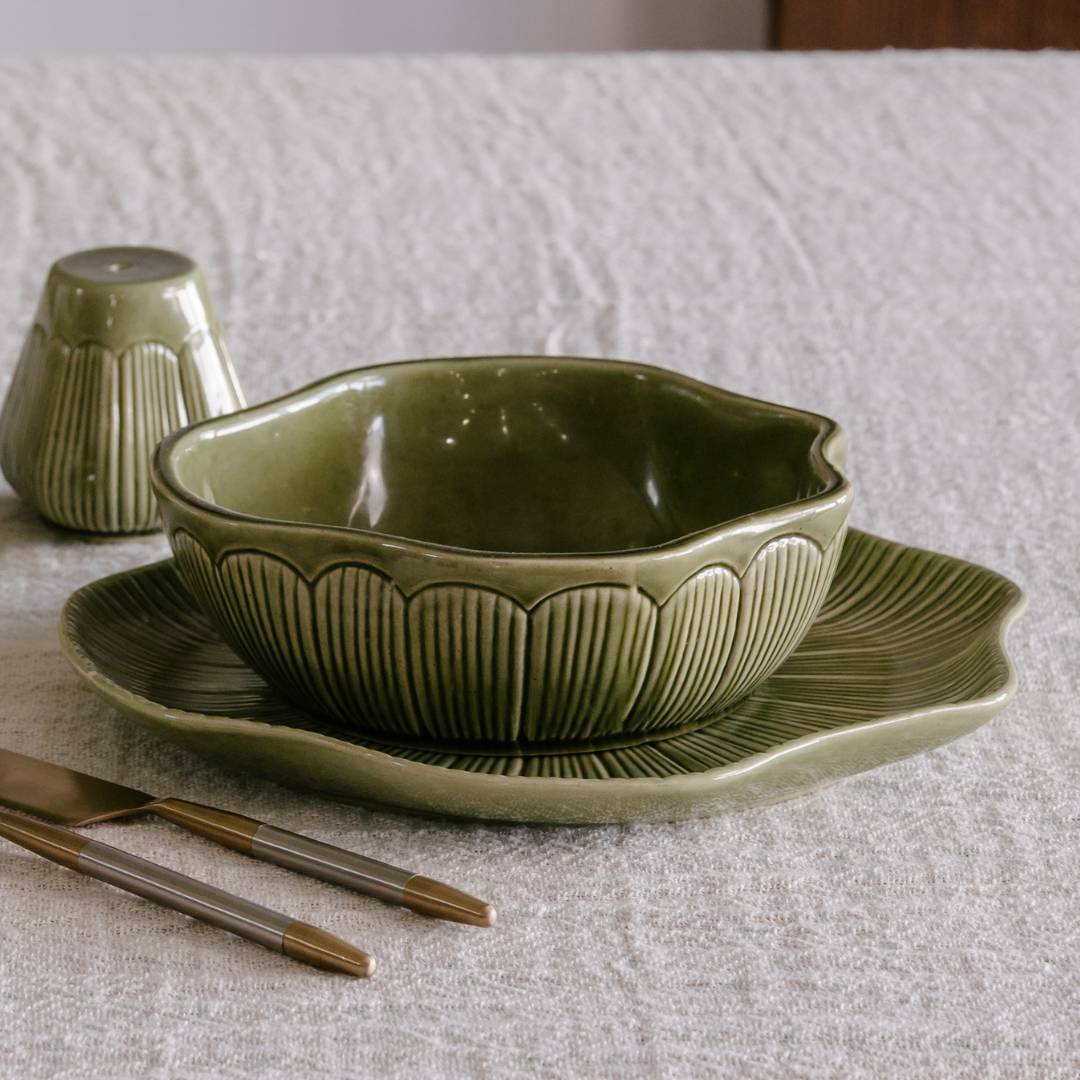 Green ceramic bowl and plate set on a textured surface with gold cutlery.