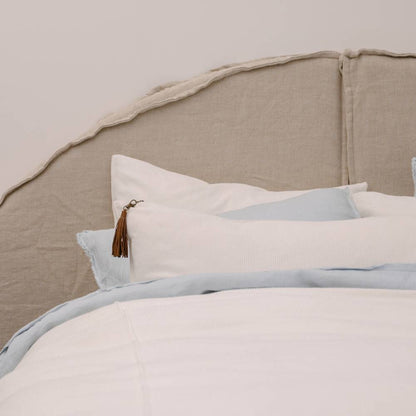 Neatly made bed with light-colored bedding and pillows against a neutral headboard.