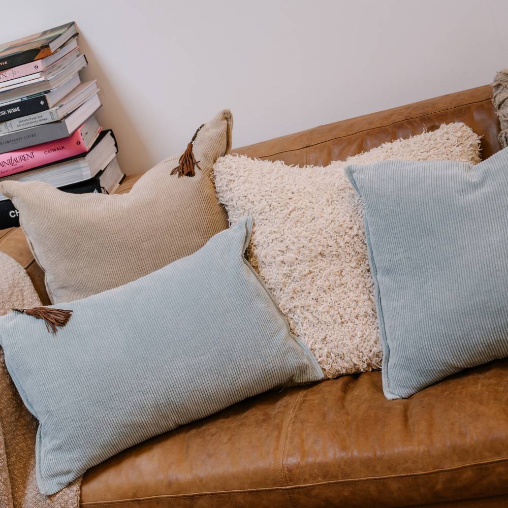 Brown leather sofa with decorative pillows and a stack of books on a white wall.