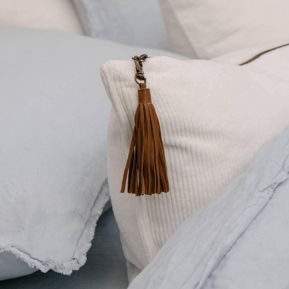 Brown tassel keychain on a textured white pillow with light blue fabric.