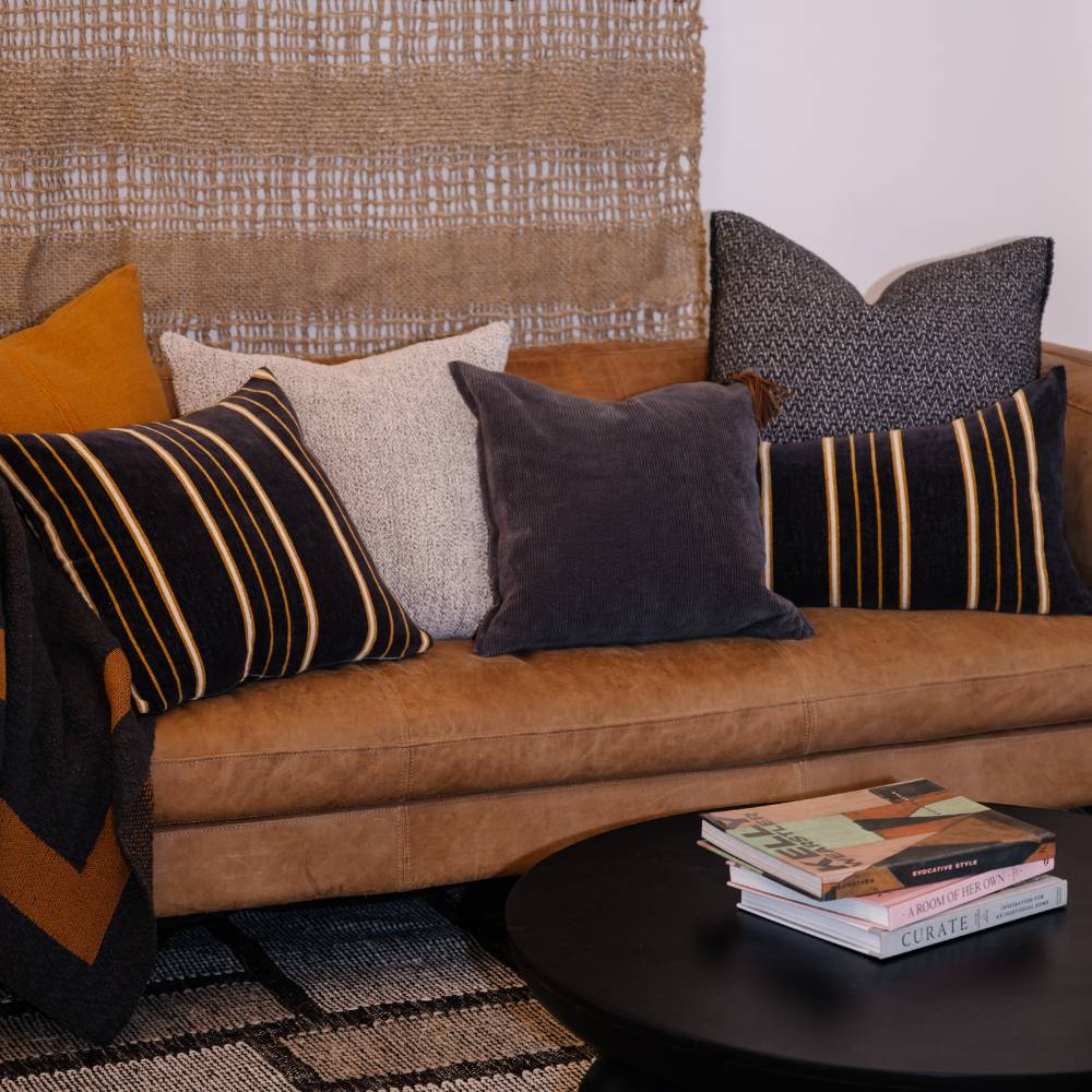 Brown sofa with patterned cushions and a stack of books on a side table.