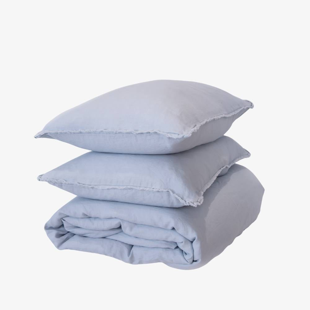 Stack of light blue bedding including a duvet and two pillows on a white background