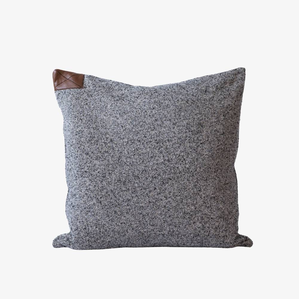 Gray textured pillow with brown leather accent on a white background