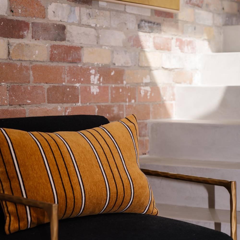 Brown striped pillow on a black sofa against a brick wall.