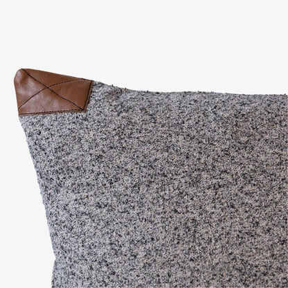 Gray textured pillow with a brown leather corner on a white background