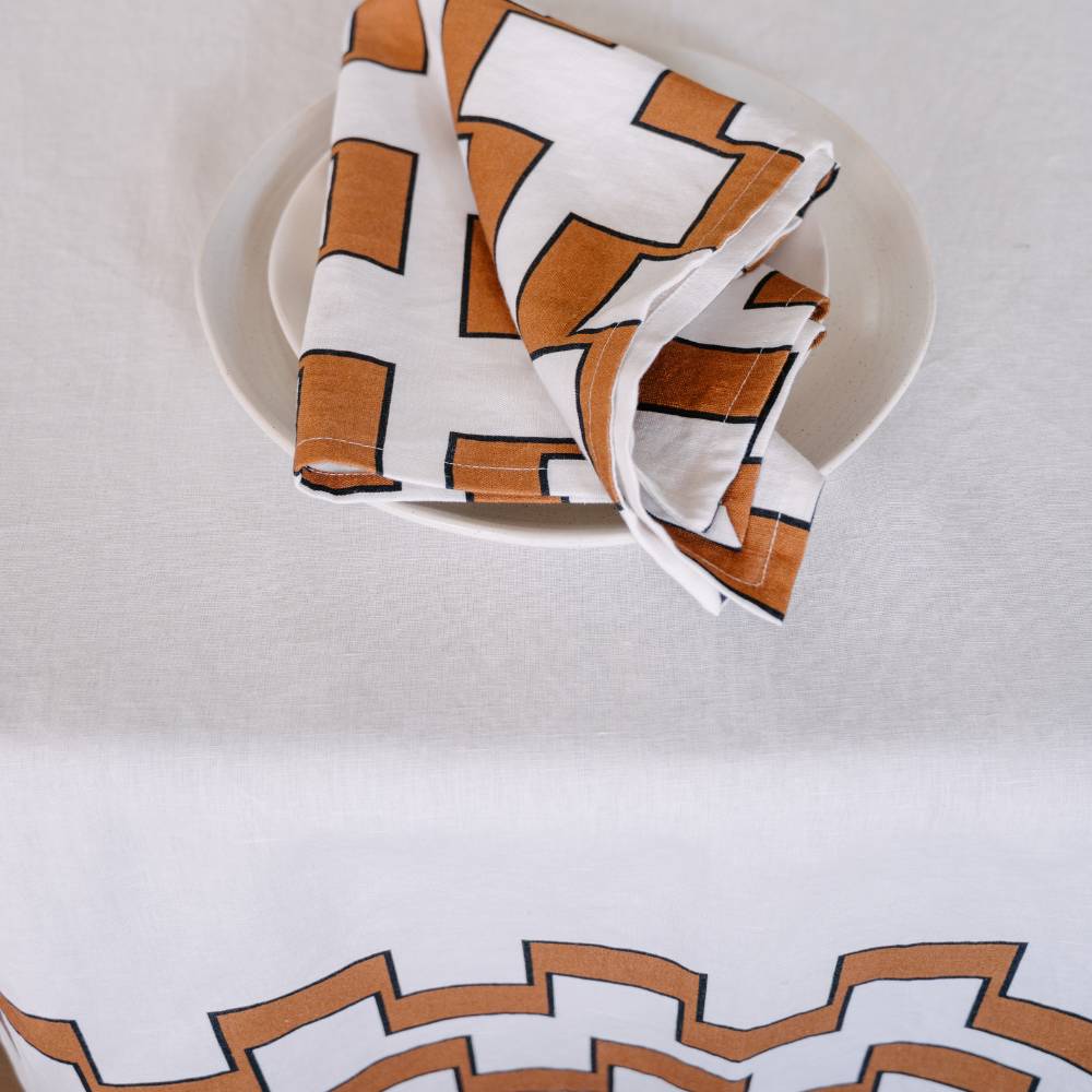 Table napkin with nutmeg geometric pattern on a white plate against a matching background
