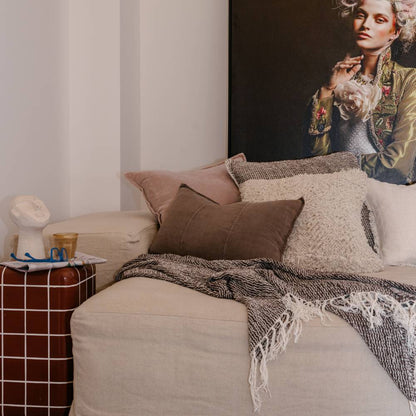 Neatly made sofa with decorative pillows and a blanket, next to a bedside table with a cup and small statue.