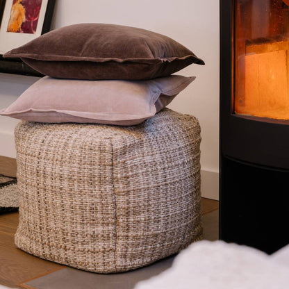 Textured ottoman with stacked cushions in a cozy room setting.