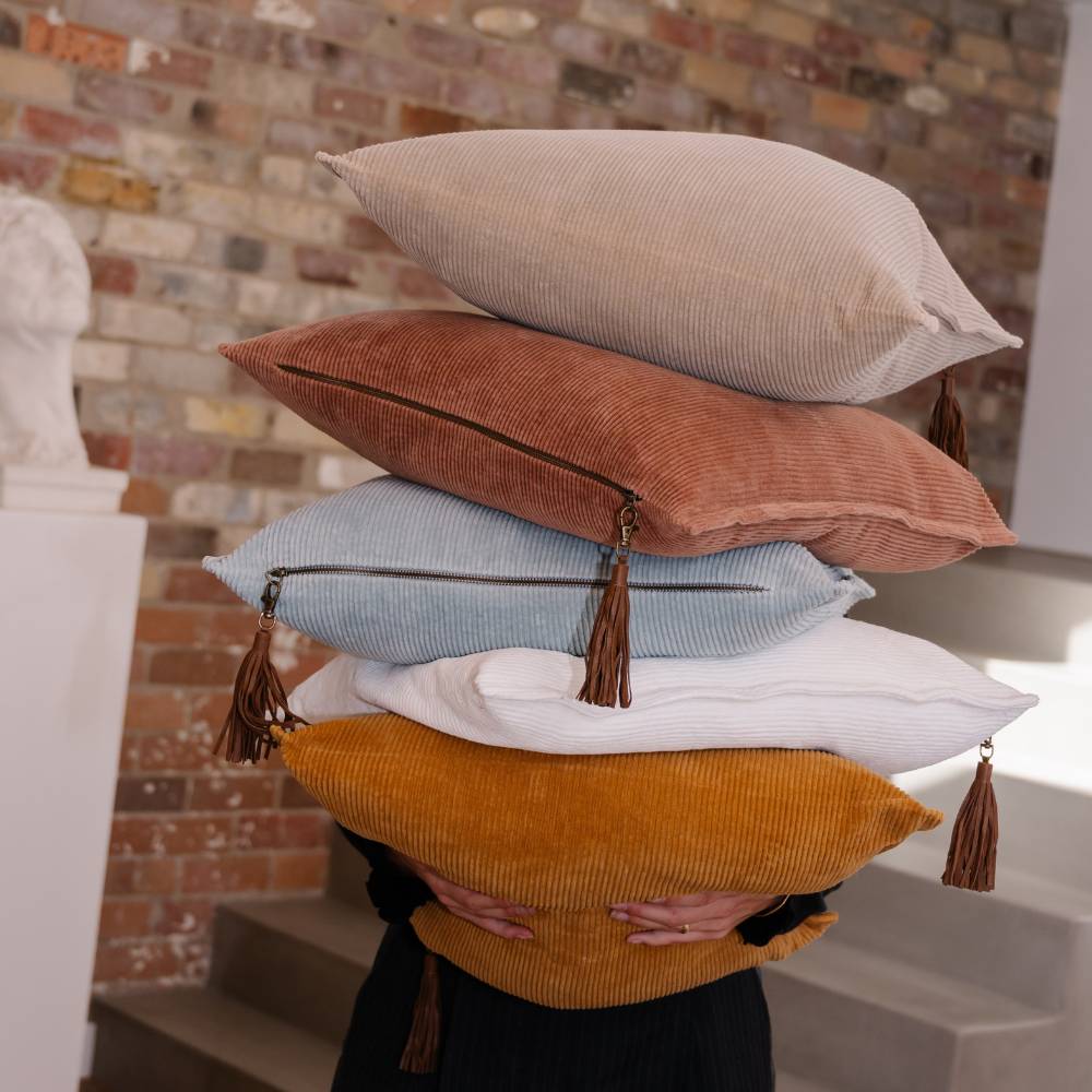Stack of colorful pillows with tassels against a brick wall.