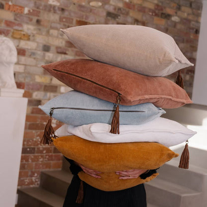 Stack of colorful pillows with tassels against a brick wall.