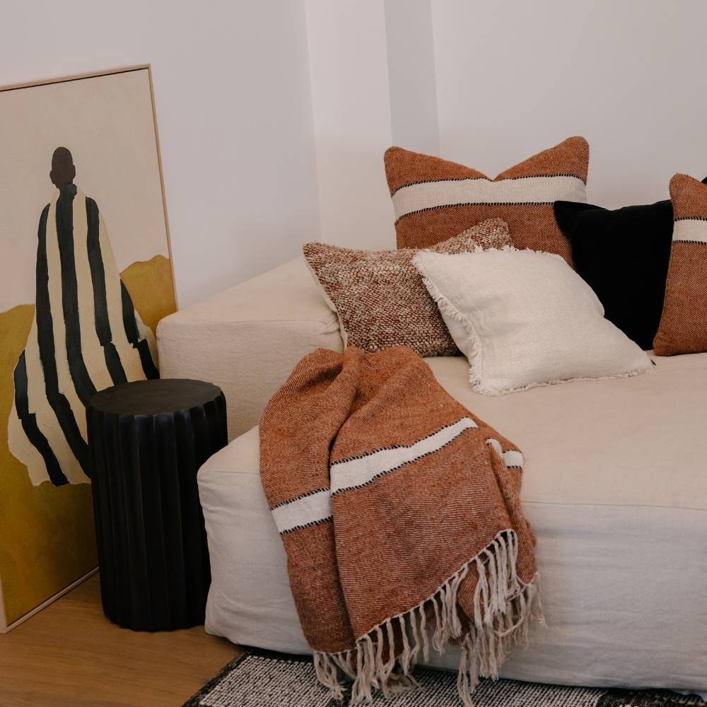 White sofa with patterned cushions and a brown throw blanket in a living room setting.