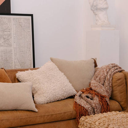 Brown sofa with decorative pillows and a blanket in a living room setting.
