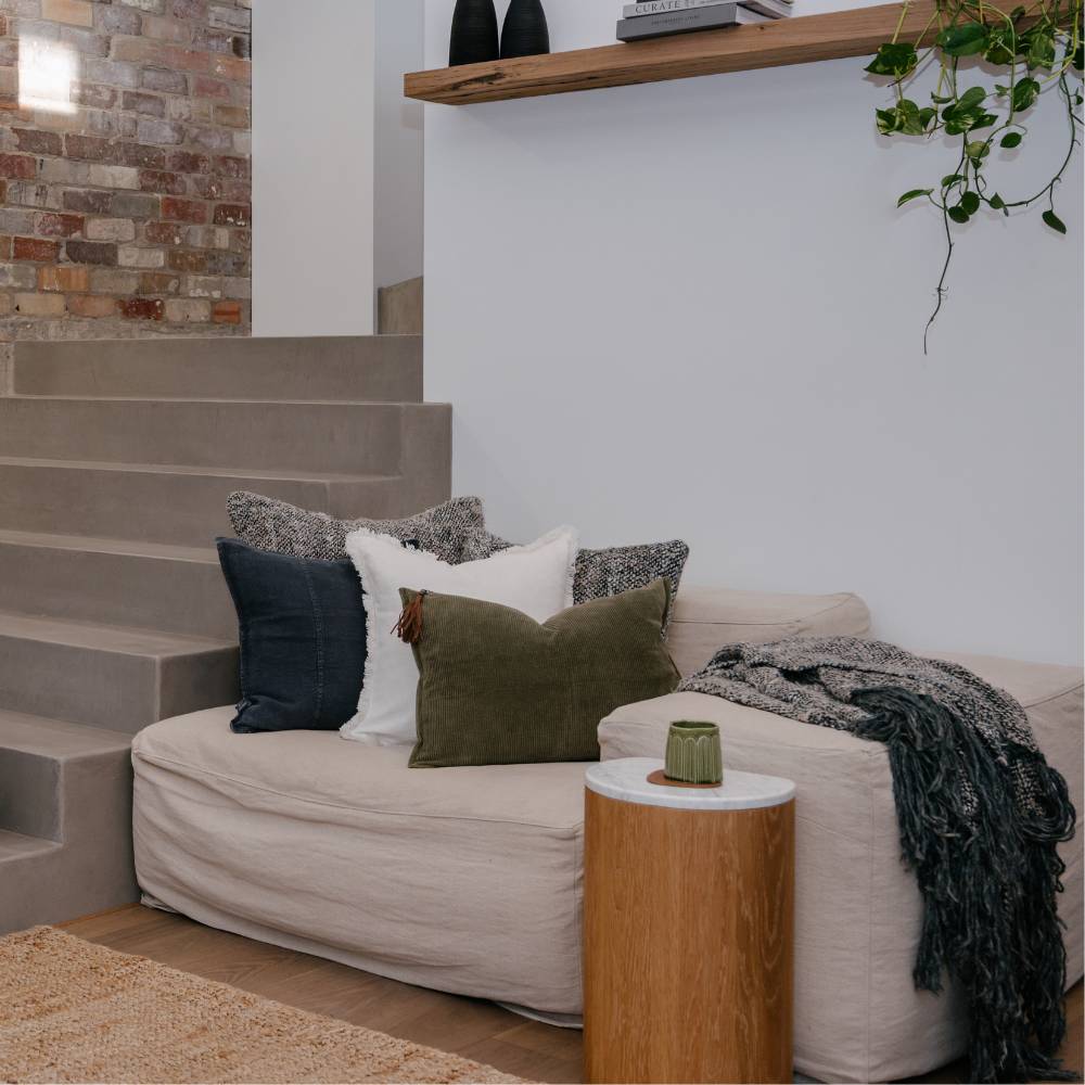 Beige sofa with decorative pillows and a wooden side table in a living room setting.