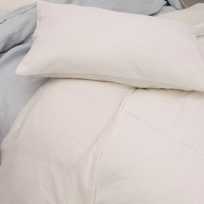 Close-up of light gray bedding with a pillow on a bed.