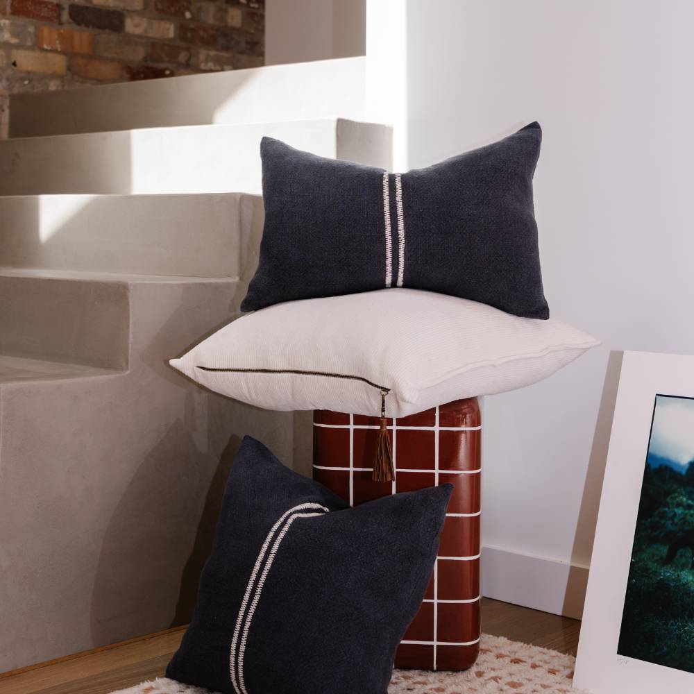 Decorative pillows on a stool against a wall with a framed picture.