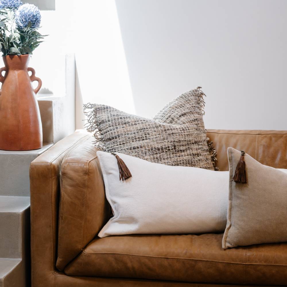 Brown leather sofa with decorative pillows and a vase of flowers on a side table.