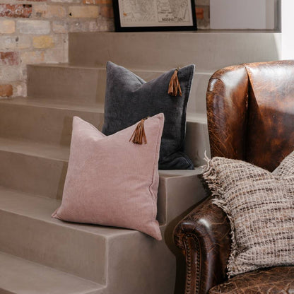 Pink and gray pillows with tassels on a staircase next to a leather chair.