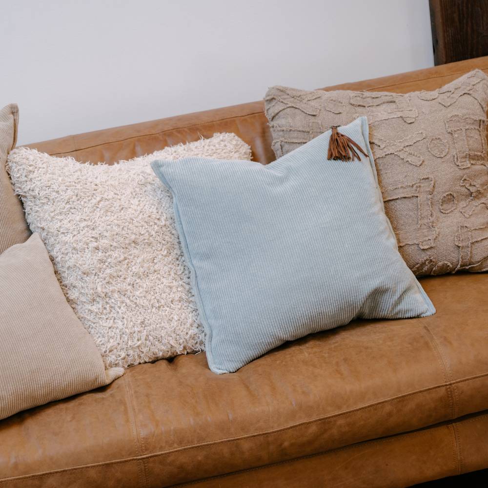 Brown sofa with decorative pillows including a textured beige, fluffy white, light blue, and patterned brown pillow.