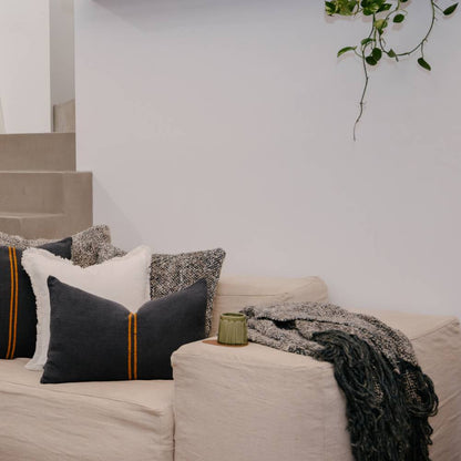 Beige sofa with decorative pillows and a blanket in a living room setting.