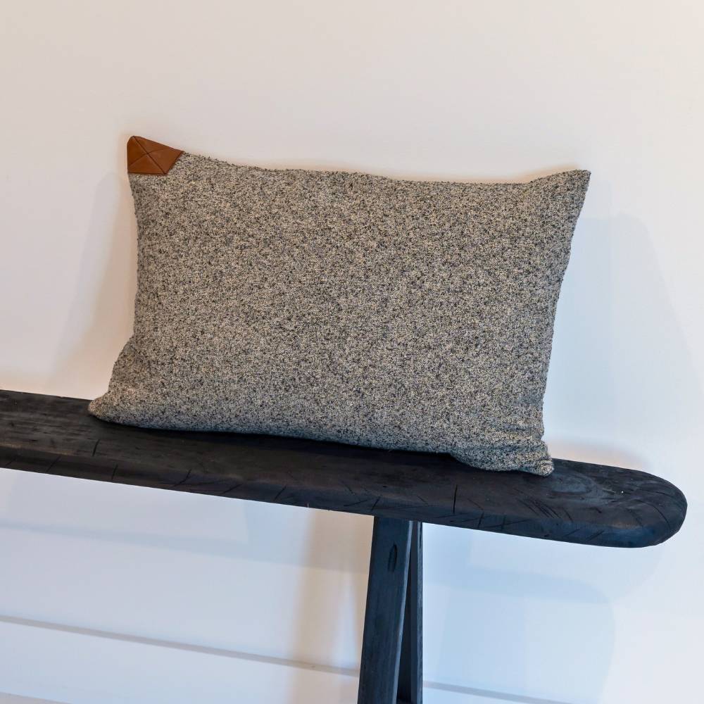 Gray textured pillow on a wooden bench against a white wall