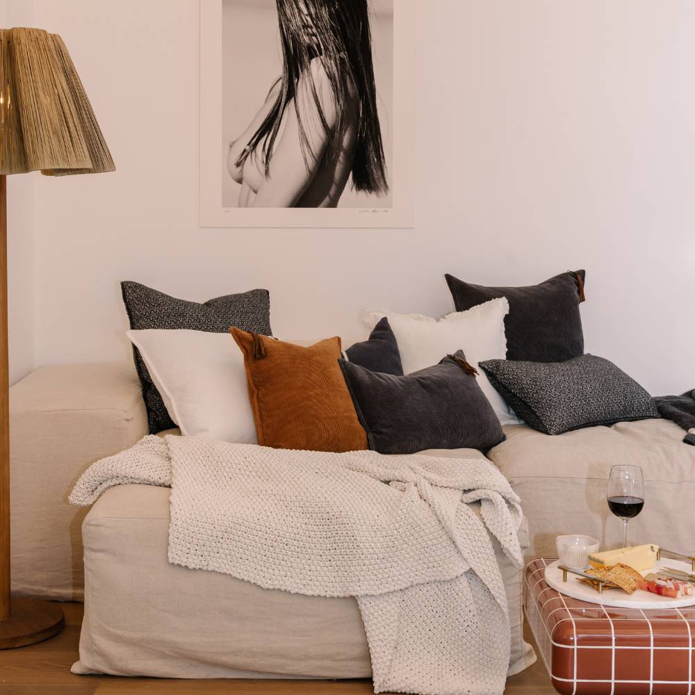 Cozy living room with a beige sofa adorned with colorful pillows, a blanket, and a small table with snacks and a glass of wine.