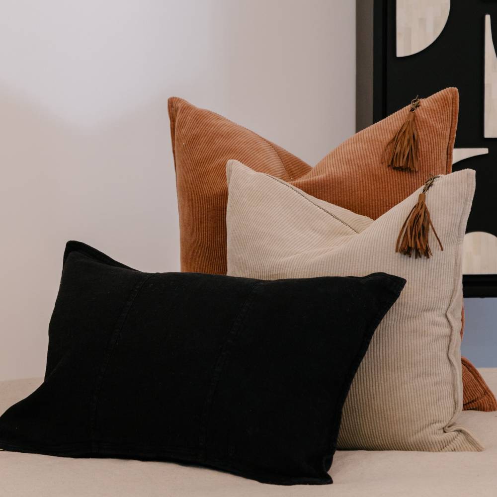 Three pillows in black, brown, and beige on a bed with a neutral background