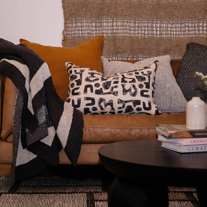 Cozy living room with a brown sofa, patterned cushions, and a side table with books.
