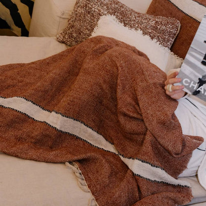 Person wrapped in a brown blanket on a couch with patterned cushions.